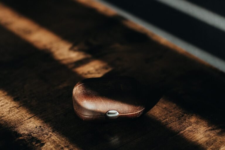 Étui AirPods marron en cuir poli sur table en bois éclairée par le soleil